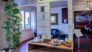 Un vestíbulo de hotel con una recepción, una gran planta de bambú, un sofá de cuero azul y certificados enmarcados en la pared.