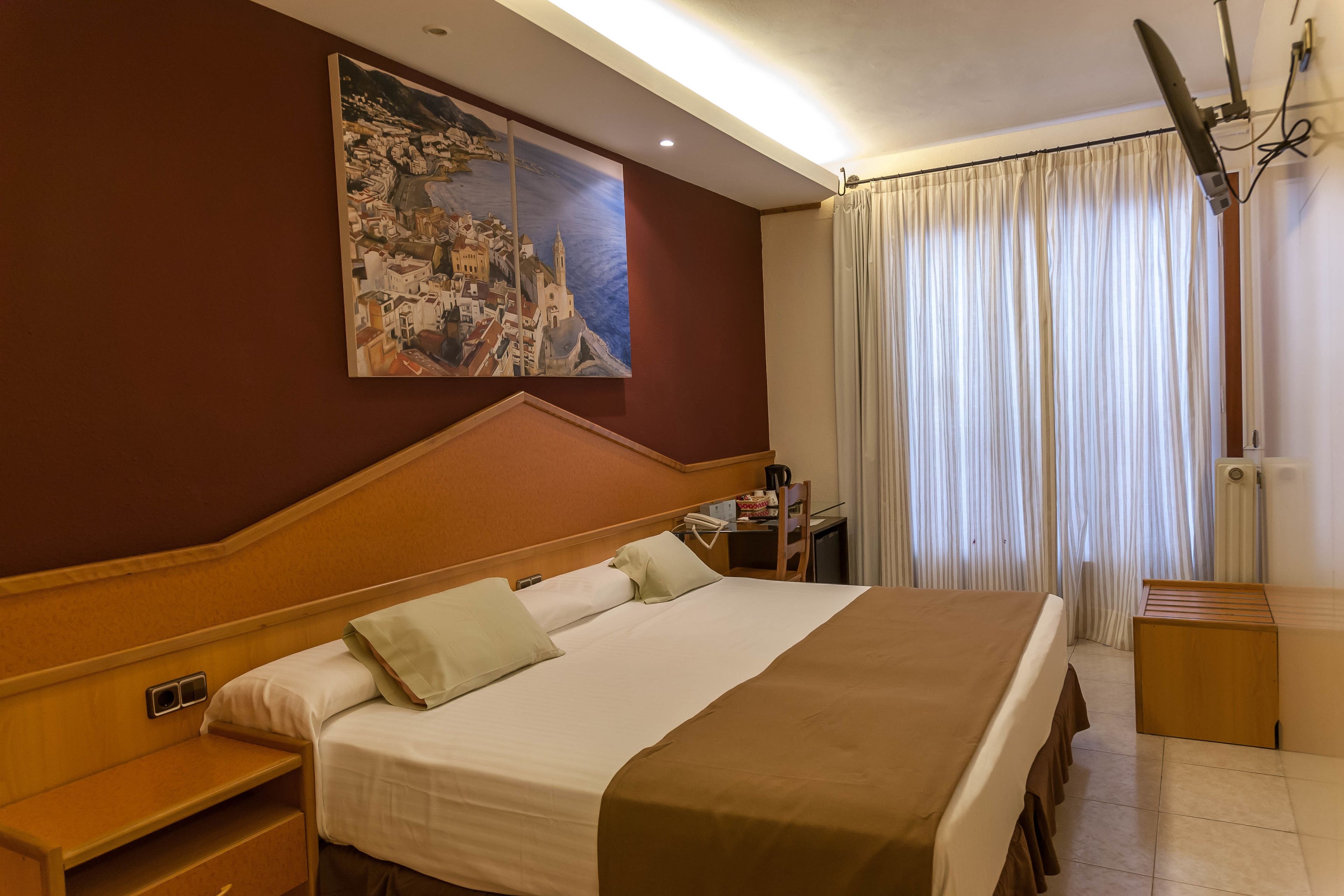 Habitación de hotel con una cama grande, un escritorio, una silla, un cuadro en la pared y una ventana con cortinas.