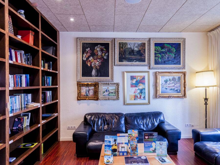 Una sala de estar con un sofá de cuero negro, una estantería de madera y obras de arte enmarcadas en la pared.