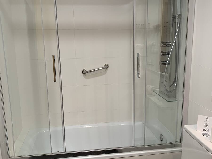 Un baño moderno con ducha de vidrio, inodoro blanco y lavamanos de acero inoxidable.