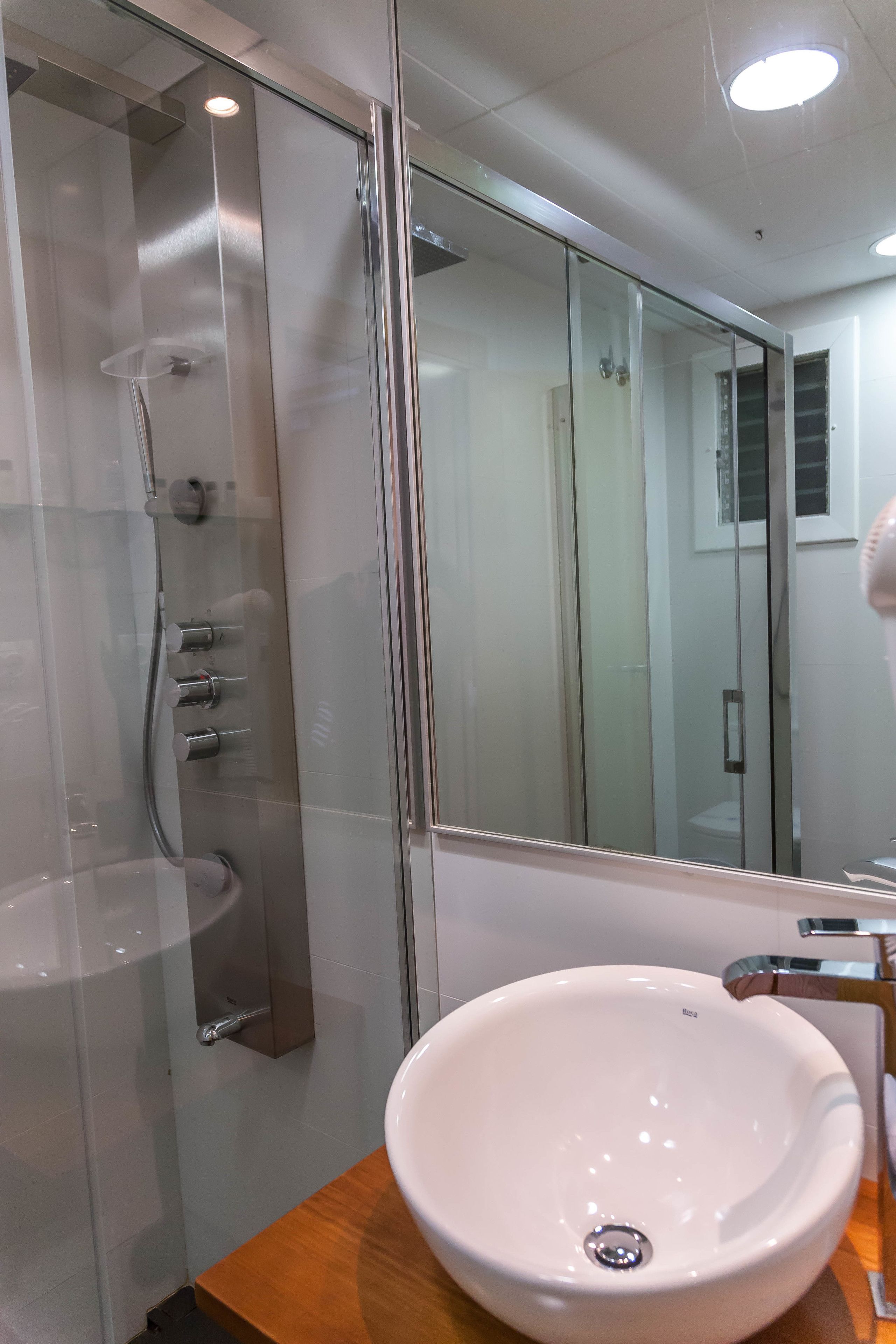Un baño moderno con ducha de vidrio, lavamanos blanco y encimera de madera.