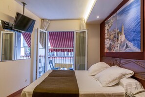 Habitación de hotel con cama, televisor montado en la pared, balcón con vistas y un cuadro en la pared.