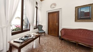 A room with a wooden bench, a red sofa, a wooden door, and a window with curtains. - Hotel Alla Fava (Venice)