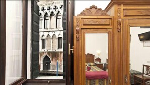 A room with a large window, a wooden door, and a bed with a red blanket. - Hotel Alla Fava (Venice)