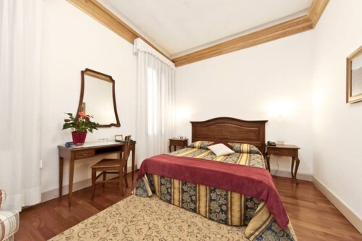 A bedroom with a wooden bed, a desk with a chair, a mirror, and a potted plant.