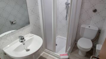 Un baño con lavamanos blanco, inodoro y ducha con mampara de vidrio.