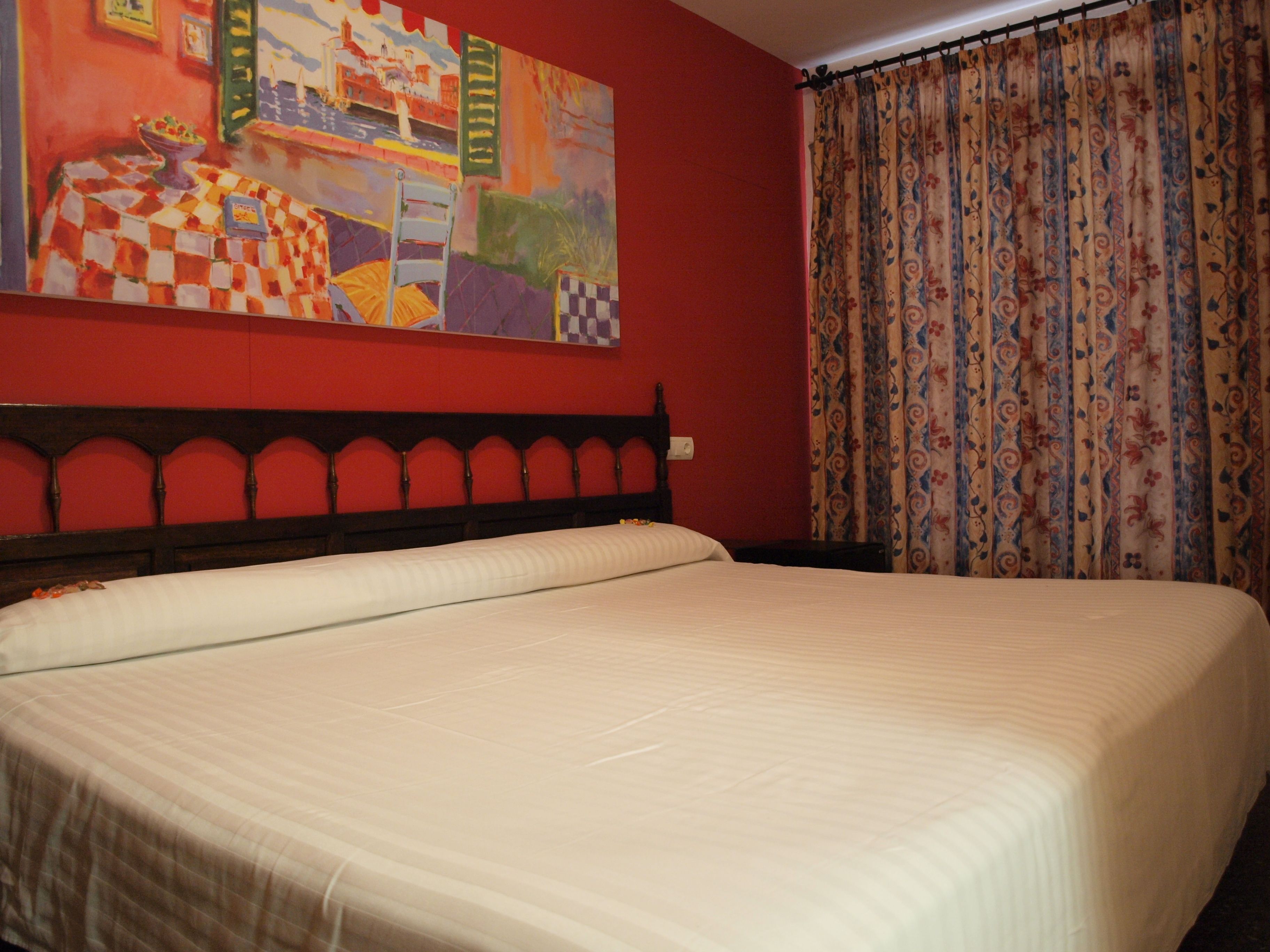 Una cama en una habitación con pared roja y un cuadro encima.