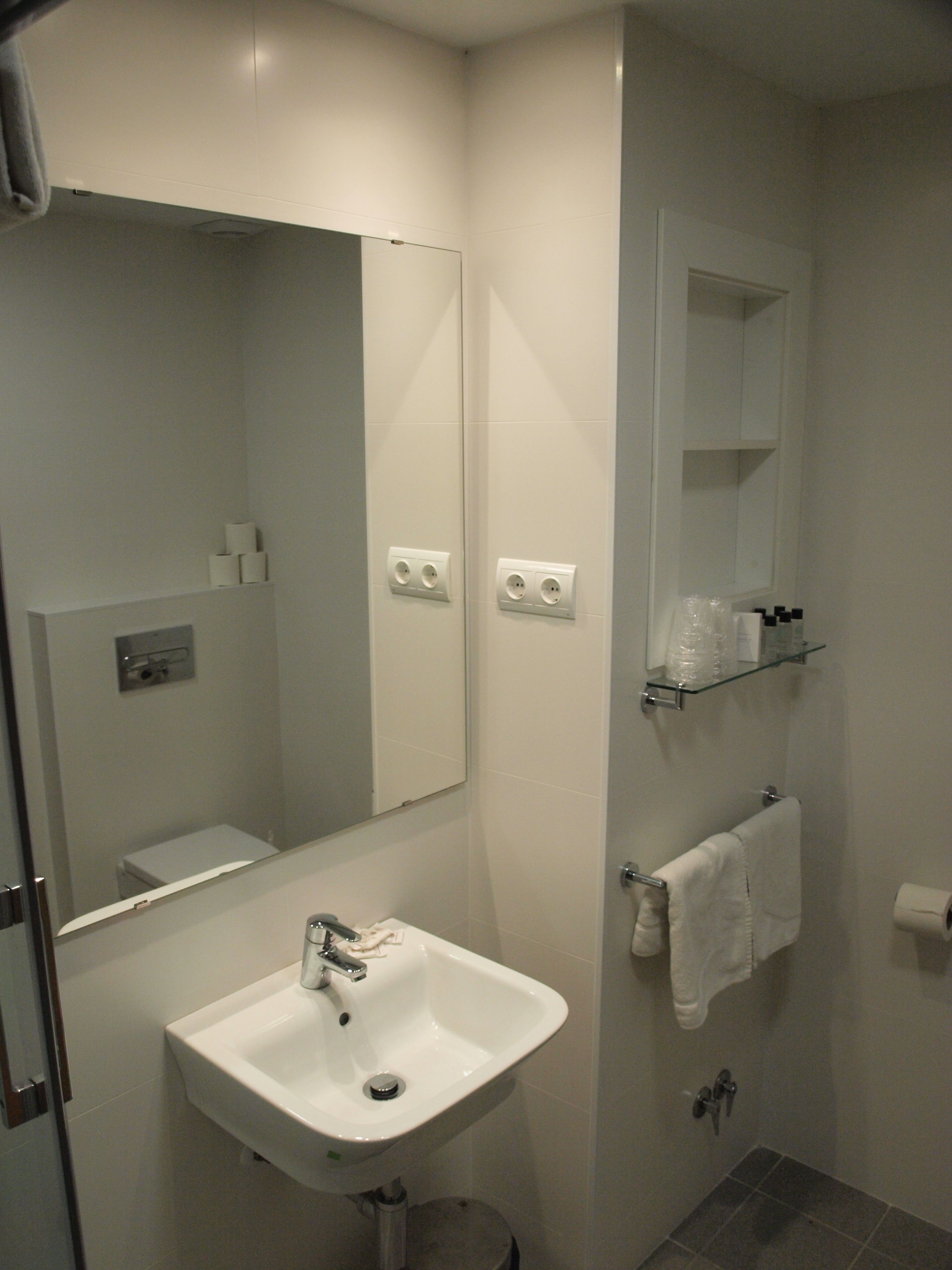 Un baño moderno con lavamanos, espejo y toallero blancos.