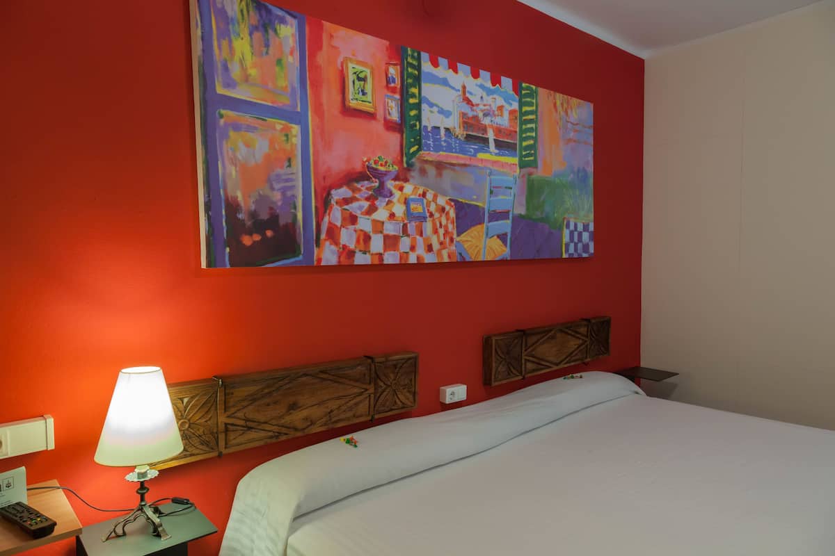 A hotel room with a large bed, a nightstand with a lamp, a painting on the wall, and a wooden headboard.