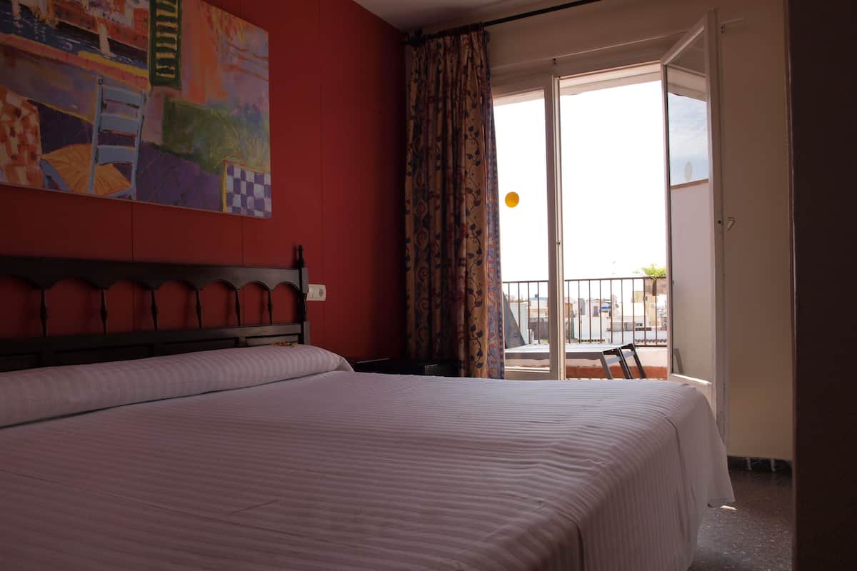 A hotel room with a large bed, a painting on the wall, and a balcony with a view.