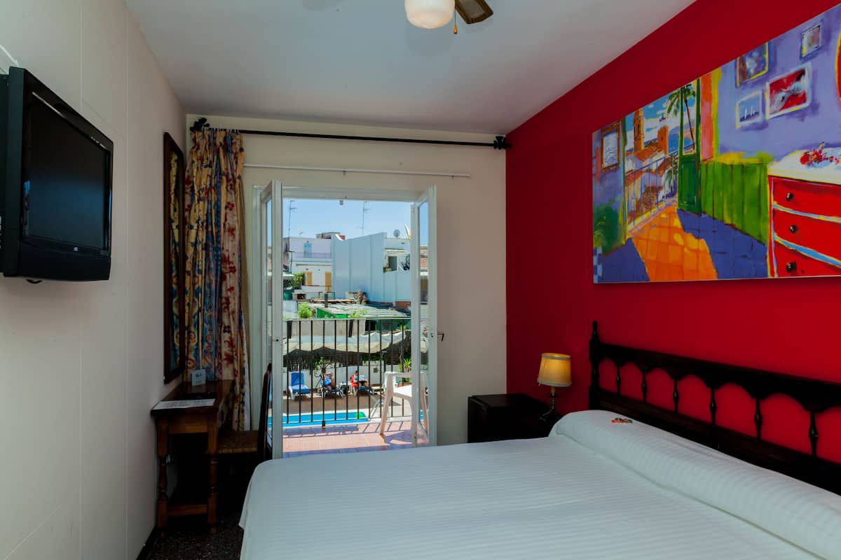 A hotel room with a bed, a TV, a painting, and a view of the outside.