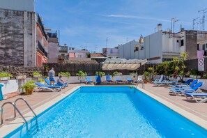 Une piscine rectangulaire, bordée d’une terrasse carrelée, entourée de chaises longues et de parasols.