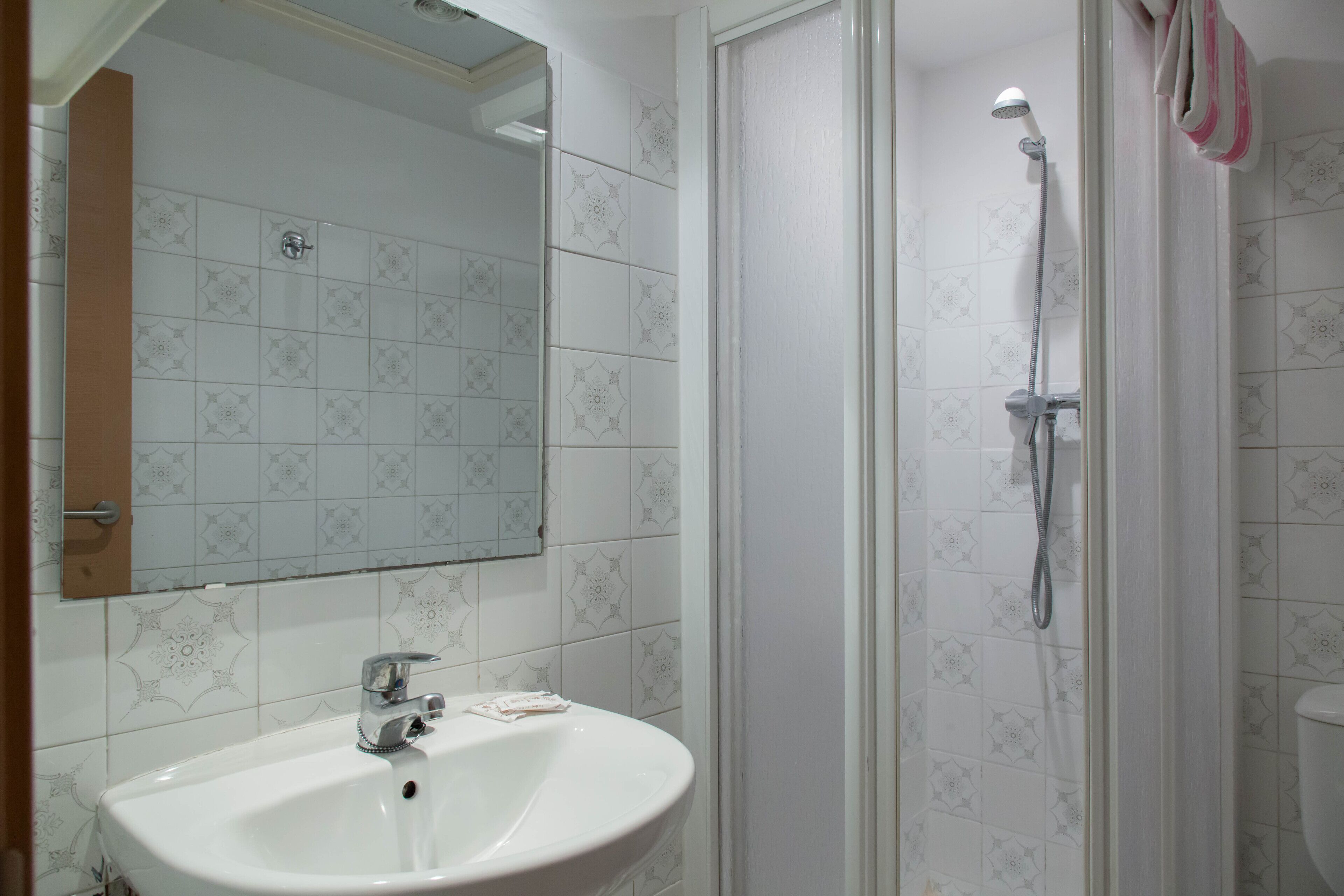 Een badkamer met een wit wastafel, een spiegel en een douche met een handdouche.