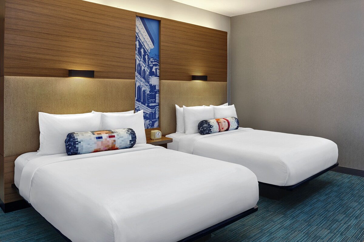 A hotel room with two beds, a large wall mural, and a modern design.