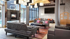 A modern lobby with a fireplace, seating area, and large windows. - Aloft by Marriott Montreal Airport (Dorval)
