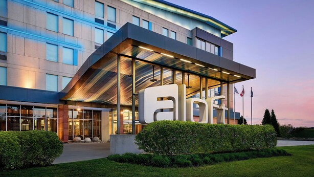A modern hotel with a prominent 'aloha' sign, large windows, and a well-lit entrance. - Aloft by Marriott Montreal Airport (Dorval)