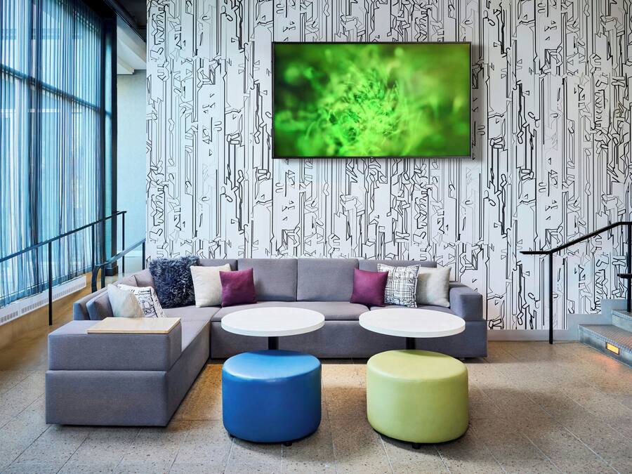 A modern lounge area with a grey sectional sofa, two round tables, and colorful ottomans. A large TV is mounted on the wall above the sofa.