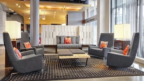 A modern lobby with grey armchairs, a central sofa, and a patterned rug. - Aloft by Marriott Montreal Airport (Dorval)