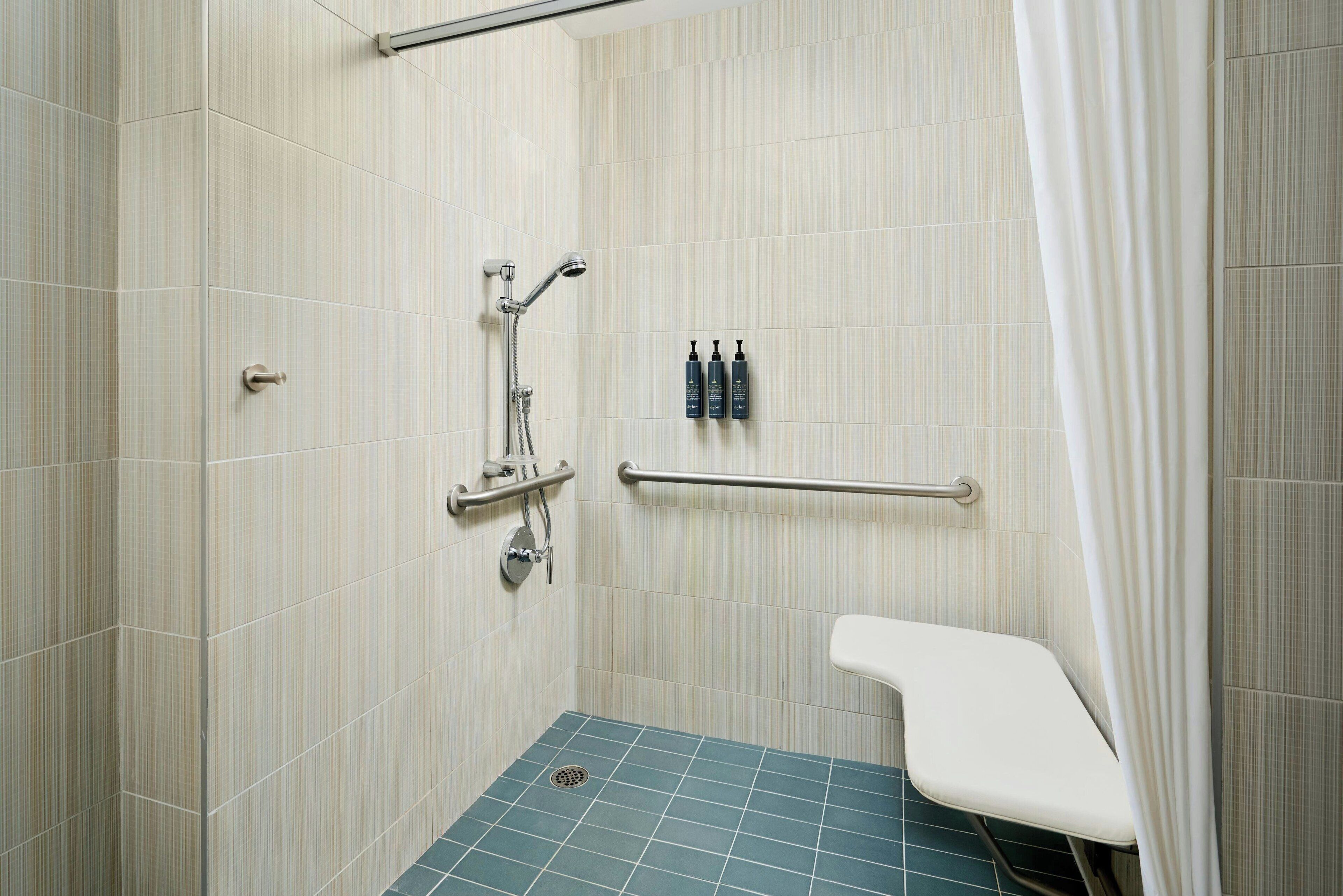 A small, tiled shower area with a grab bar, a showerhead, and a bench.