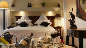 Une chambre d’hôtel avec un grand lit, un lustre, une petite table avec une lampe, une statue et une horloge fixée au mur.