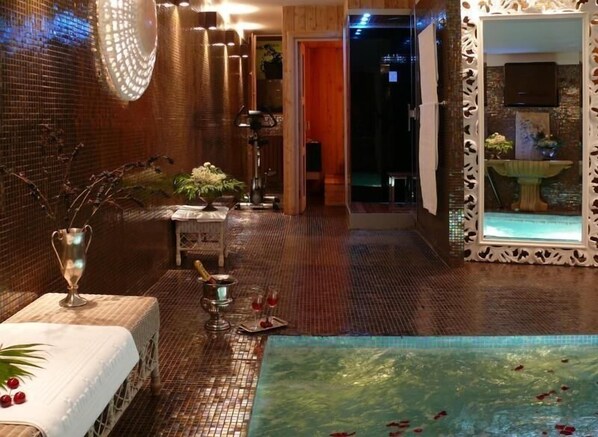 Un espace spa doté d’un sol carrelé, d’une petite table avec un vase et une bouteille, d’un miroir décoratif et d’une vue sur une piscine.