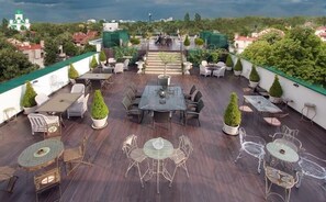 Une terrasse sur le toit, dotée de nombreuses tables et chaises, entourée de plantes en pot et offrant une vue sur le paysage urbain.