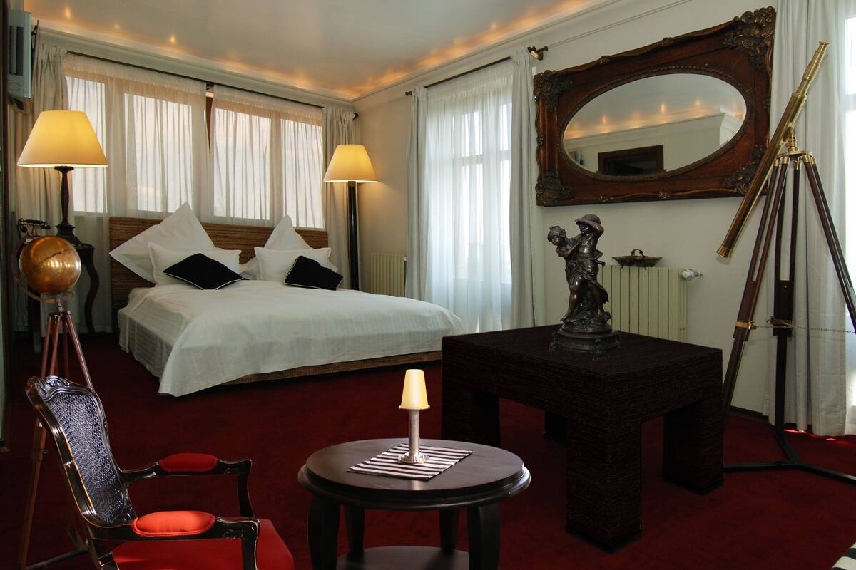 Une chambre d’hôtel avec un grand lit, deux lampes de chevet, un globe terrestre posé sur un trépied, une statue sur une table et un télescope.