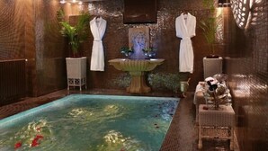 Un espace spa comprenant un jacuzzi, deux peignoirs blancs suspendus à un porte-peignoirs, une petite fontaine et une table dressée avec une bouteille et des verres.