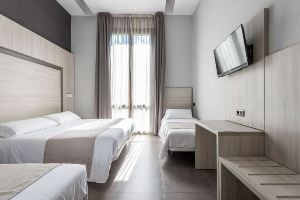 Habitación de hotel con dos camas, un televisor montado en la pared y una ventana con cortinas.