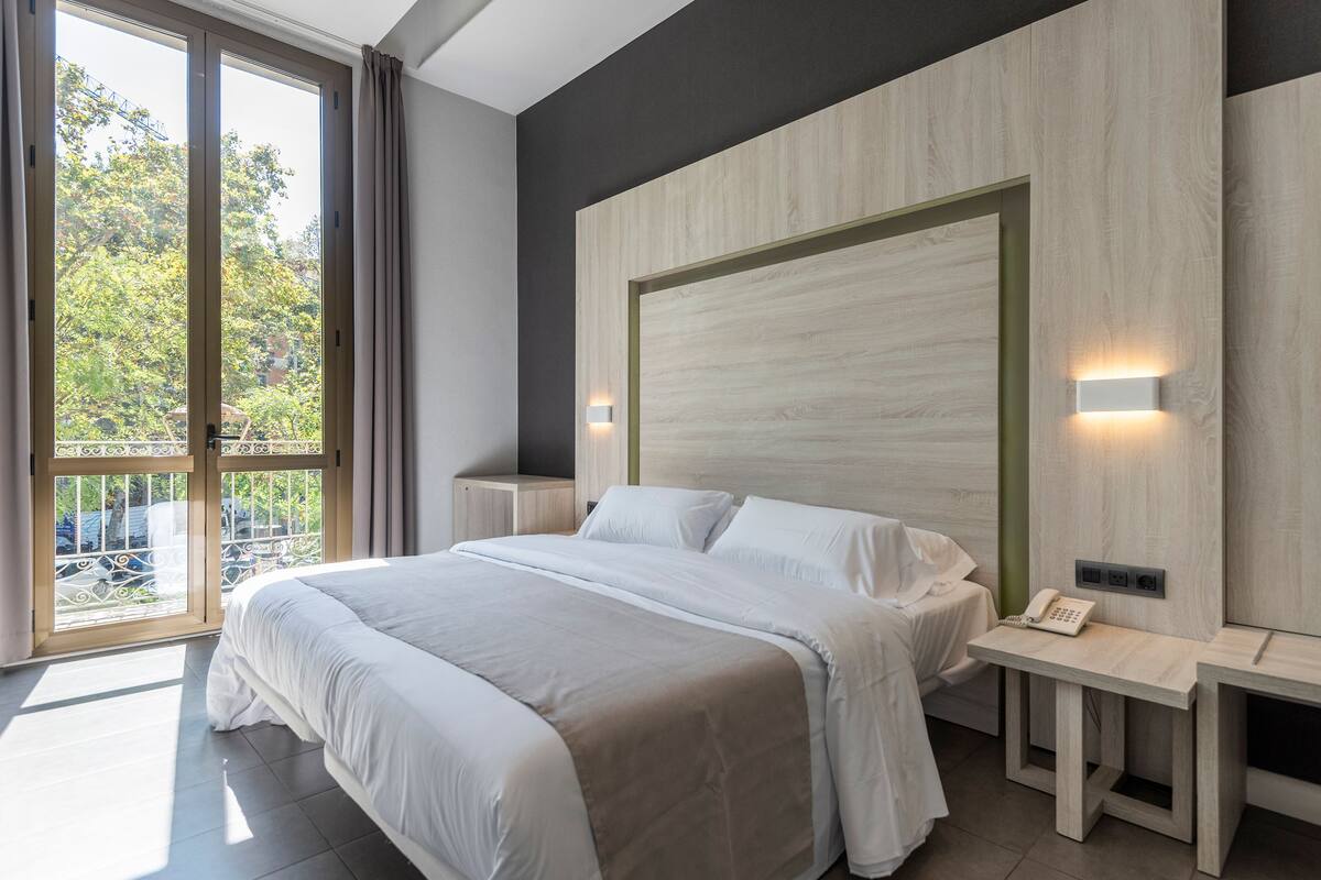 Een moderne slaapkamer met een groot bed, een nachtkastje en een uitzicht op de omgeving door middel van een schuifdeur.