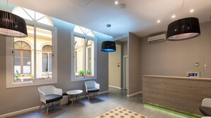 A reception area with a reception desk, two chairs, a patterned rug, and a large window with a view of a courtyard. - Plaza Goya Rooms (Barcelona)