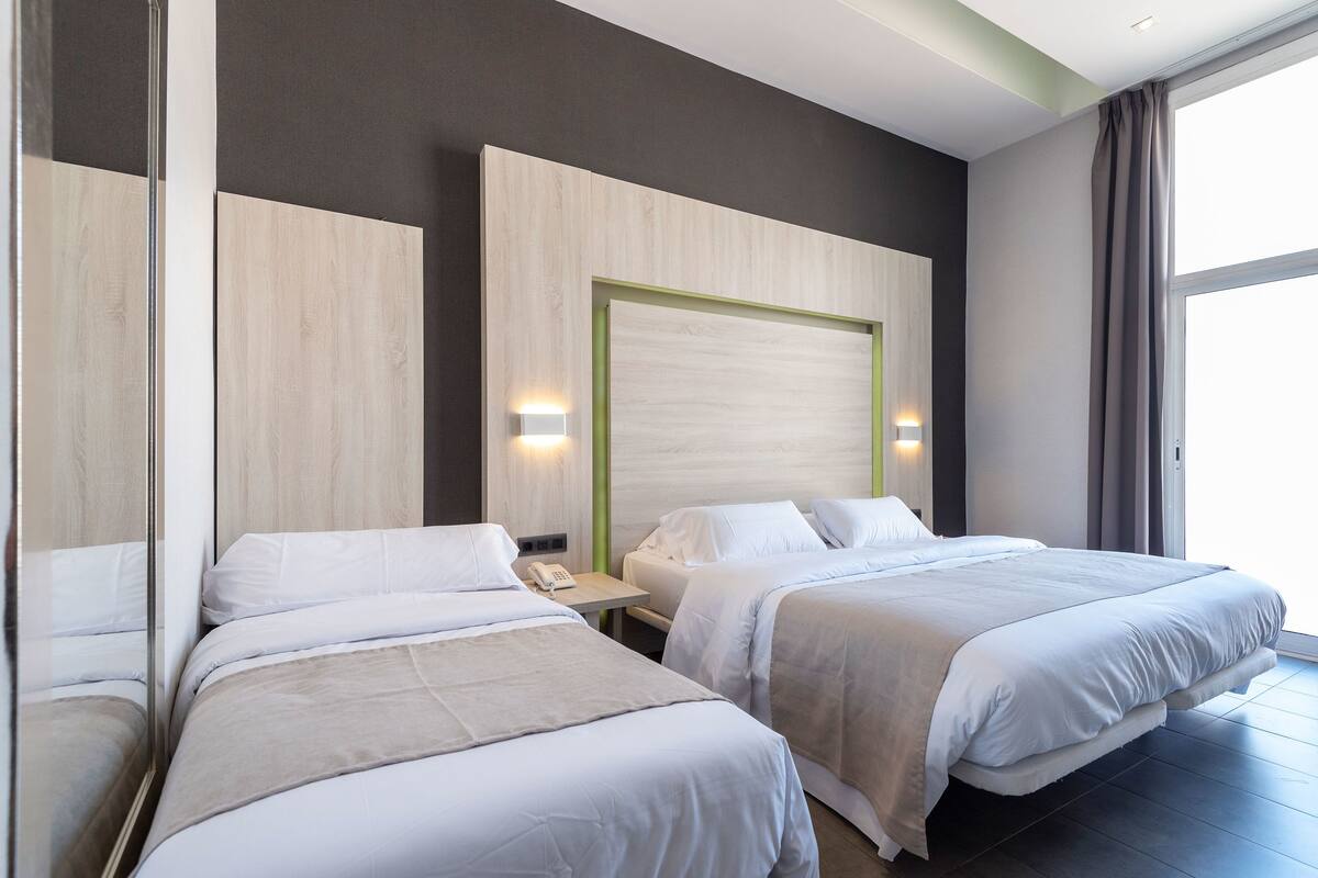 Een hotelkamer met twee bedden, een nachtkastje met telefoon en een groot raam met gordijnen.