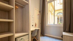 A hotel room with a wooden desk, a chair, a built-in safe, and a window with curtains. - Plaza Goya Rooms (Barcelona)