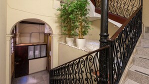 A staircase with ornate black metal railings, a potted bamboo plant, and a white tiled floor. - Plaza Goya Rooms (Barcelona)