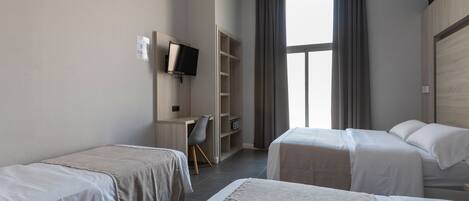 Une chambre d’hôtel avec deux lits simples, un bureau avec une chaise, une télévision et une grande fenêtre avec des rideaux.