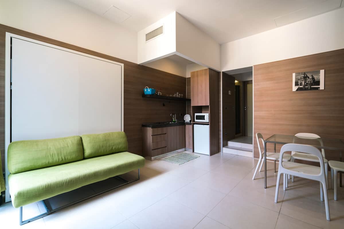 Un espacio habitable compacto con un sofá verde, una zona de cocina y una mesa de comedor con sillas.