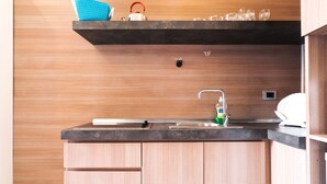 A modern kitchen with wooden cabinets, a black countertop, a stainless steel sink, and a shelf above the sink holding a kettle, glasses, and a blue towel. - Residence Europa (Rome)