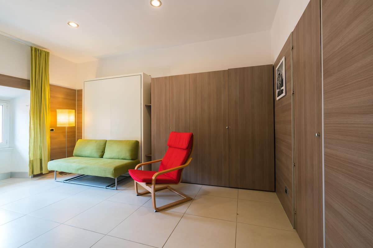 Habitación de hotel moderna con sofá verde, una silla roja, paneles de pared de madera y suelo de baldosas.