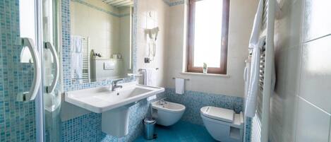 Un baño con lavamanos, bidé e inodoro, con azulejos azules y blancos.