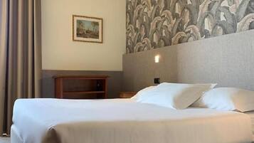 Una habitación de hotel con una cama grande, una mesita de noche, un cuadro enmarcado en la pared y un papel tapiz estampado.