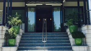 L’entrée d’un hôtel, avec un escalier couvert, une enseigne indiquant « HÔTEL GARDENIA » et des plantes en pot de chaque côté.