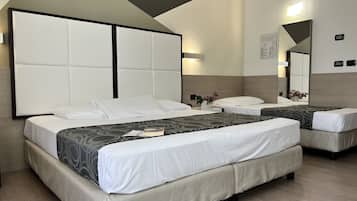 Ein Hotelzimmer mit zwei Betten, einem breiten, gepolsterten Kopfteil, einem Nachttisch mit Blumenvase und einem Spiegel an der Wand.