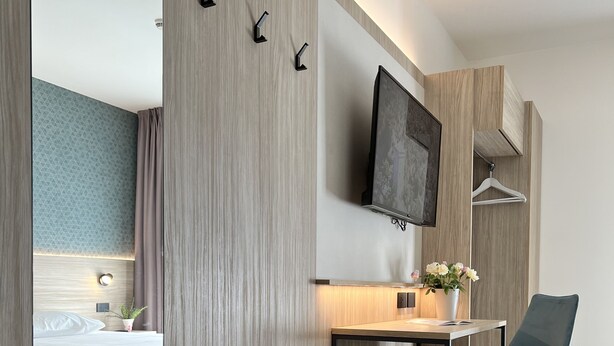 Une chambre d’hôtel moderne équipée d’un lit, d’un bureau, d’une chaise et d’un téléviseur fixé au mur.