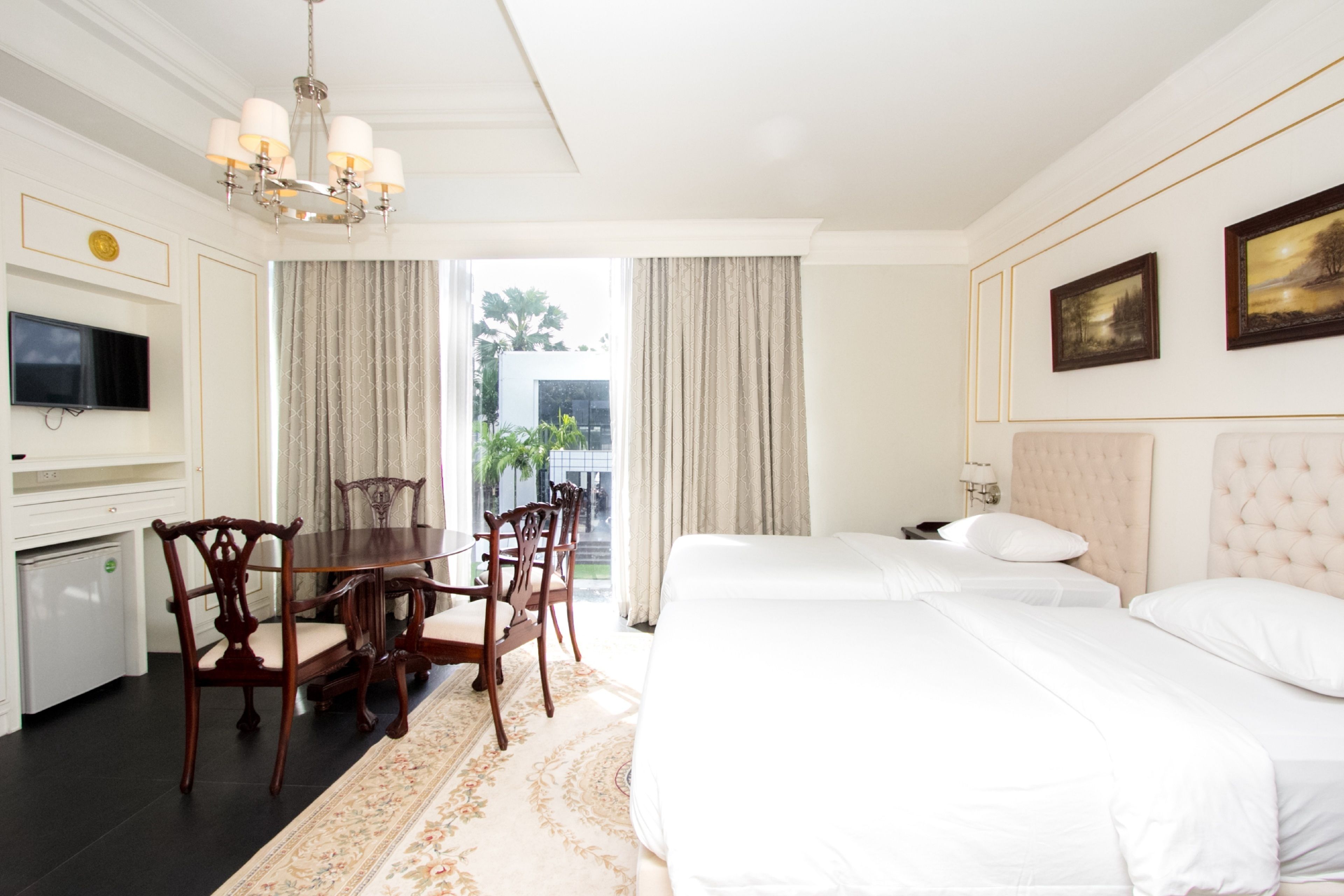 A hotel room with a dining area, two beds, a TV, and a view of the outdoors.