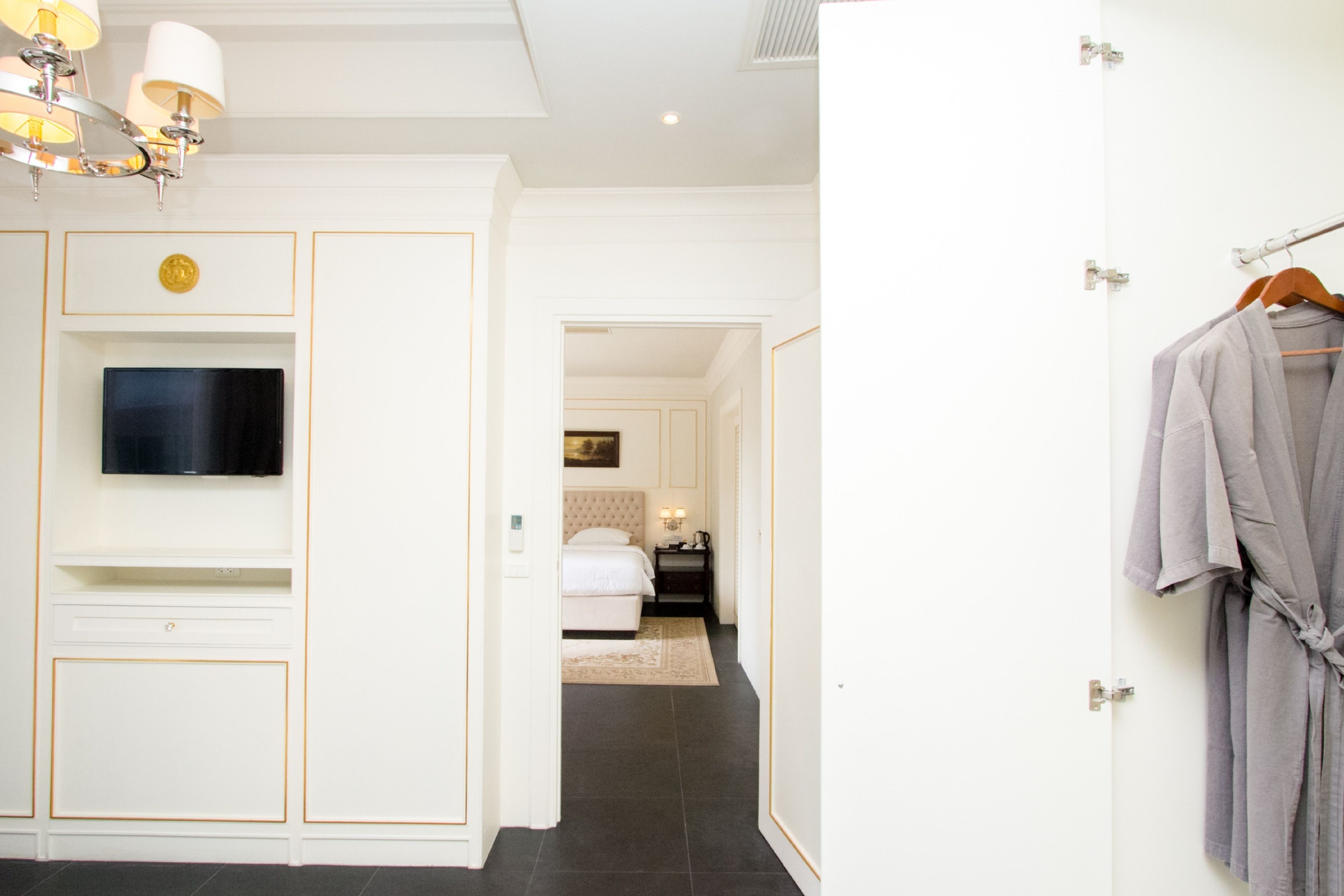 A hotel room with a flat-screen TV mounted on a white cabinet, a bed with a white headboard, and a robe hanging on a door.