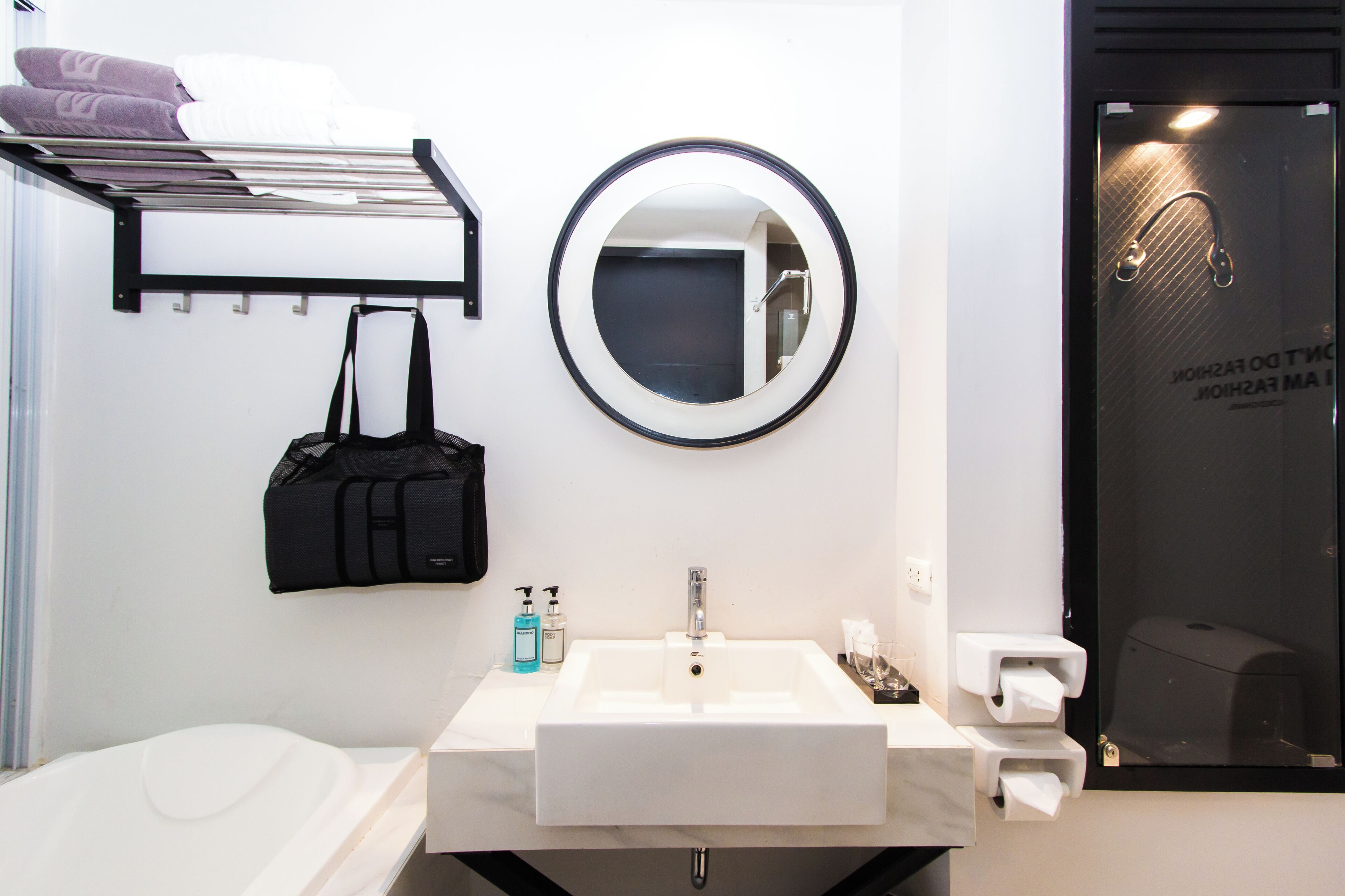 A modern bathroom with a white sink, a round mirror, a towel rack, and a black bag hanging on the wall.