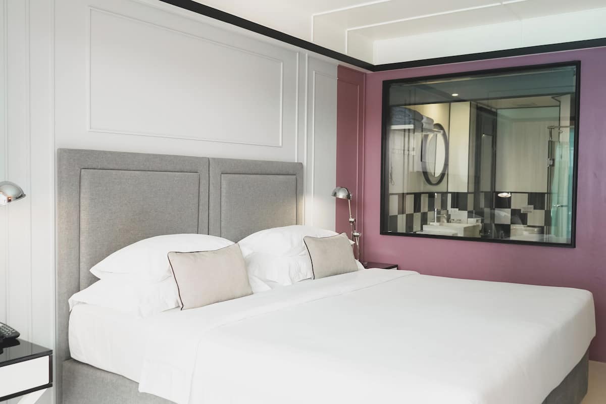Una habitación de hotel moderna con una cama grande, una mesita de noche con lámpara y un espejo en la pared.