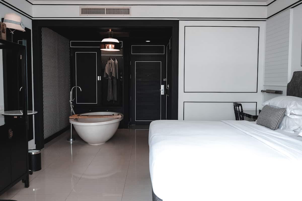 Una habitación de hotel moderna con una cama grande, una bañera independiente, un armario y una puerta que da a un baño.