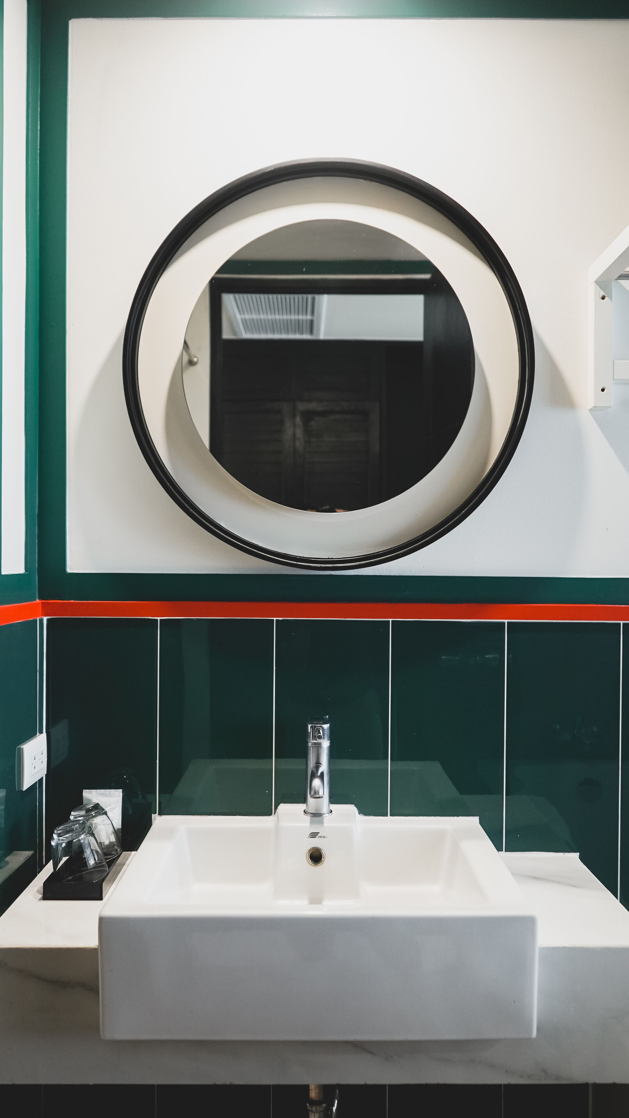 A bathroom with a white sink, a mirror above it, and green and red tiles.