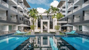 Un hotel moderno con piscina central, varios balcones y zonas de estar al aire libre.